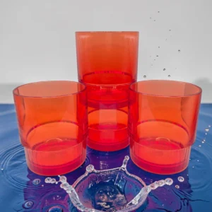 Cuatro vasos redondos de plástico color naranja apilados sobre fondo con agua