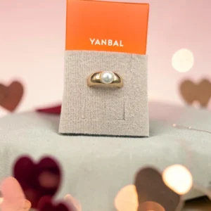 Anillo dorado con perla central, marca Yanbal, sobre exhibidor de cartón