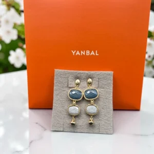 Aretes Yanbal dorados con piedras azul y blanco, exhibidos frente a su caja original.
