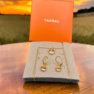 Collar con dije y candongas doradas Yanbal sobre exhibidor, con caja de la marca de fondo.