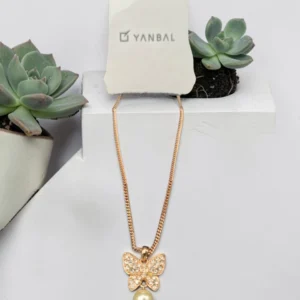 Collar dorado Yanbal con dije de mariposa y perla, sobre fondo con suculentas.