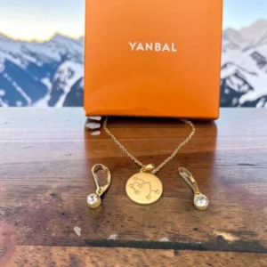 Collar y aretes dorados Yanbal con medalla de constelación, sobre caja naranja de la marca
