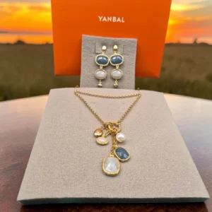 Collar y aretes Yanbal con dijes en tonos azul y blanco sobre exhibidor, caja Yanbal de fondo