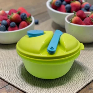 Portacomidas redondo verde con tapa azul y cuchara, junto a bowls de fresas y arándanos