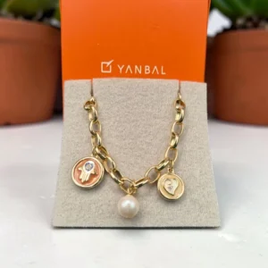 Pulsera dorada Yanbal con dijes de mano, corazón y perla, sobre exhibidor y caja de marca