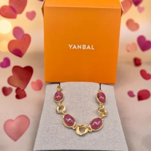 Pulsera Yanbal con dijes rosados y eslabones dorados sobre exhibidor, junto a caja de la marca.