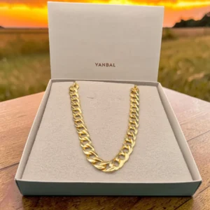 Collar dorado de eslabones gruesos sobre caja Yanbal, fondo de atardecer.