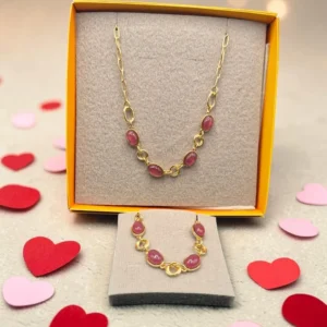 Collar y pulsera dorados con piedras rosadas, presentados en caja sobre fondo con corazones decorativos.
