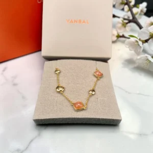 Collar Yanbal dorado con dijes coral sobre almohadilla, junto a su caja original.