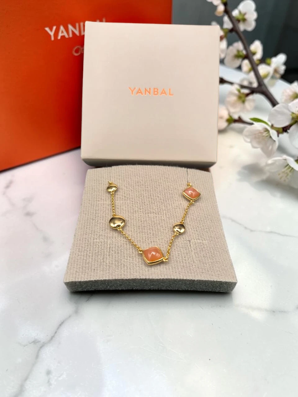 pulseradorada Collar Yanbal dorado con dijes coral sobre almohadilla, junto a su caja original.