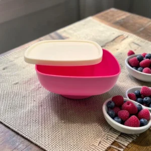 Bol hermético rosado con tapa beige sobre mesa de madera, junto a bowls con frutos rojos