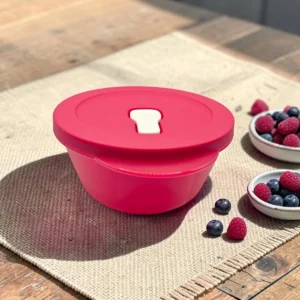 Bol hermético redondo rojo con tapa sobre mantel, junto a frutos rojos