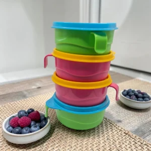 Set de cuatro tazas alimentadoras apiladas con tapas de colores y asas, sobre mesa con frutos rojos