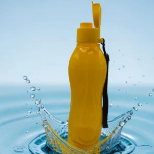 Botella plástica amarilla con tapa abatible y correa, sobre fondo de agua salpicando.