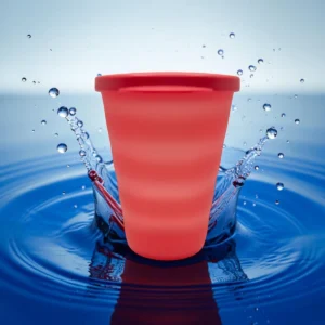 Vaso rojo con tapa sobre fondo de agua azul con salpicaduras