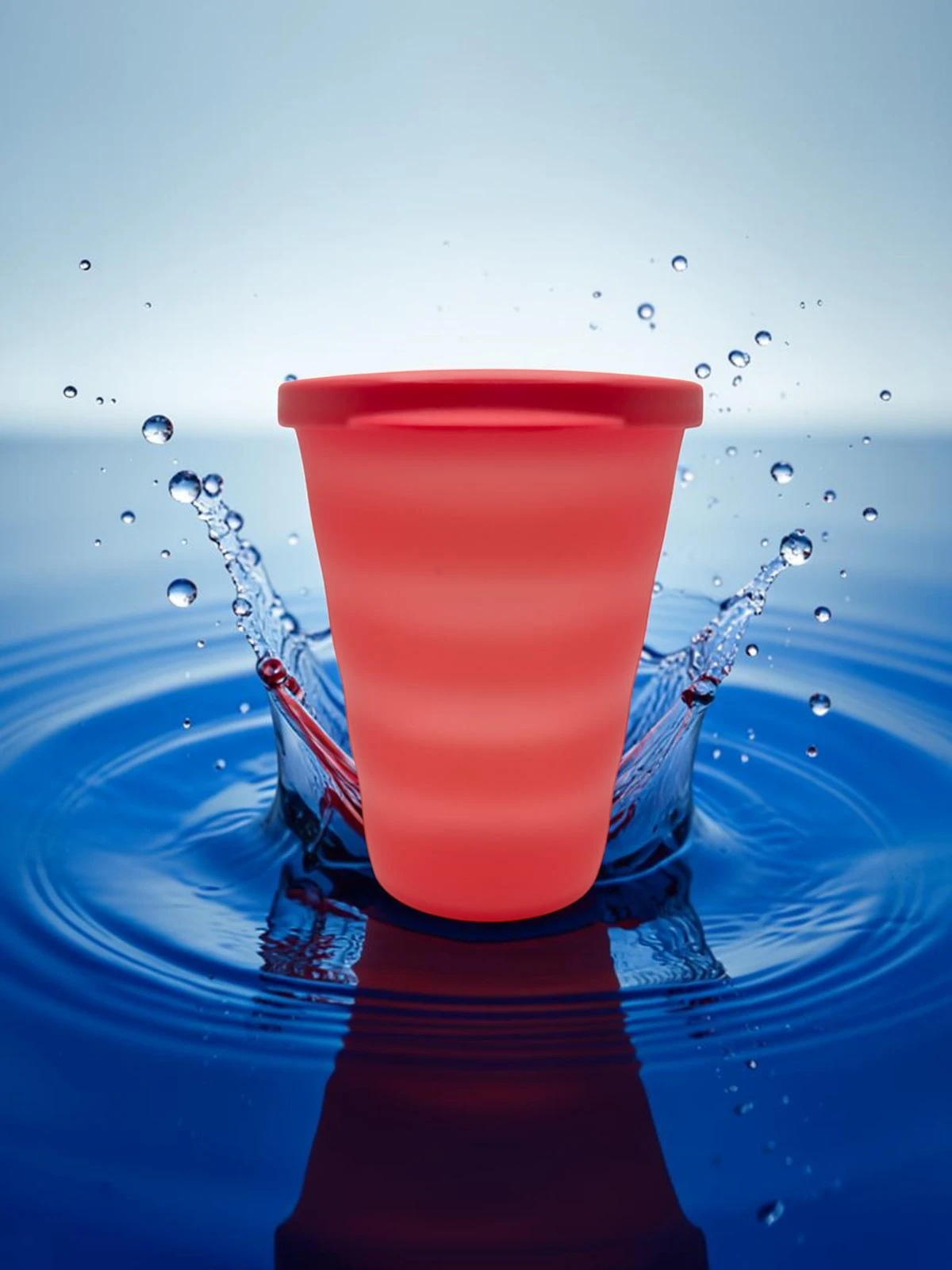 vasorojo Vaso rojo con tapa sobre fondo de agua azul con salpicaduras