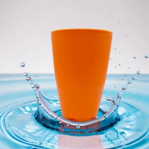 Vaso plástico naranja sobre superficie con agua salpicando