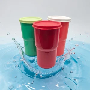 Tres vasos con tapa hermética en verde, rojo y blanco sobre agua con salpicaduras.