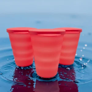 Tres vasos rojos con tapa sobre superficie con agua