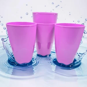 Cuatro vasos plásticos color fucsia sobre superficie con agua y salpicaduras